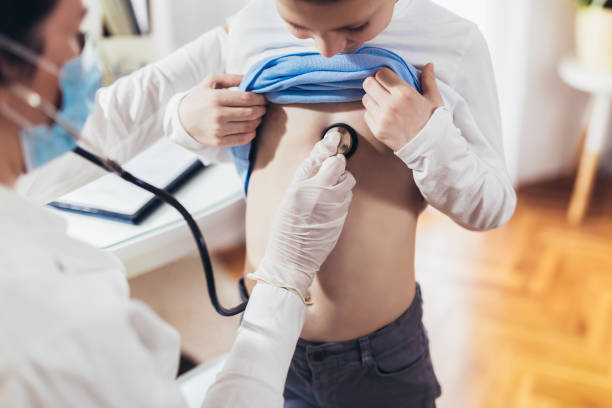 Doctor listening to boy's chest with stethoscope in his office at the hospital stock photo