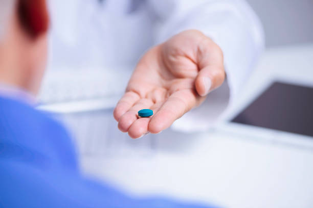 doctor man giving a blue pill to a senior man closeup of a caucasian doctor man, in a white coat, giving a blue pill to a senior caucasian patient man, sitting both at a doctors desk anti impotence tablet stock pictures, royalty-free photos & images