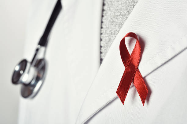 doctor man with a red ribbon closeup of a young caucasian doctor man with a pink ribbon pinned in the flap of his white coat, in solidarity of people living with HIV/AIDS world aids day stock pictures, royalty-free photos & images