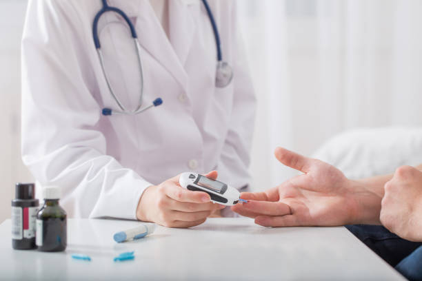 doctor measuring blood sugar young men - diabetes stock photos and pictures