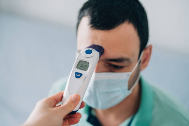 Doctor measuring body temperature with digital thermometer. Healthcare worker checking body temperature of a young sick man with contactless digital infrared thermometer. fever photos stock pictures, royalty-free photos & images