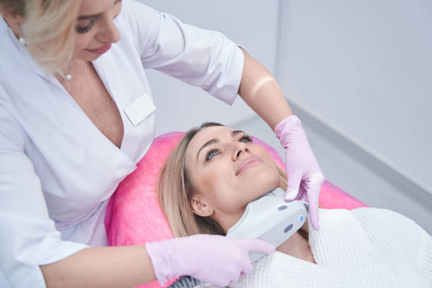 Doctor pressing ultrasonic device against woman chin during cosmetic procedure stock photo