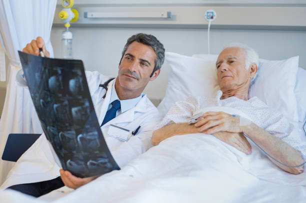 Doctor showing patient xray Senior doctor explaining xray to patient lying on hospital bed. Surgeon showing radiology report to old man admitted to hospital. Male doctor take care of his patient. x ray plates stock pictures, royalty-free photos & images