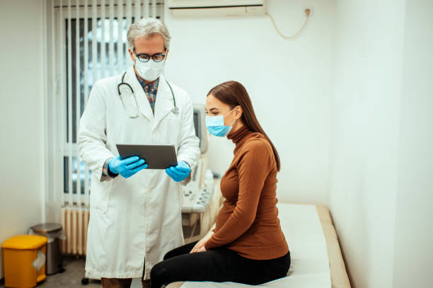 Doctor showing ultrasound pictures to pregnant woman Male OB/GYN showing ultrasound pictures to a pregnant woman with a digital tablet. Doctor and patient are wearing face masks during medical consultation. obstetrician photos stock pictures, royalty-free photos & images