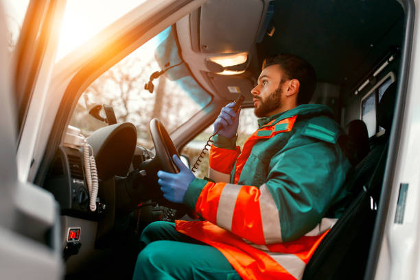 Doctor team. Medicine. An adult handsome male paramedic is talking on a portable radio while sitting in an ambulance outside a clinic. emergency response stock pictures, royalty-free photos & images
