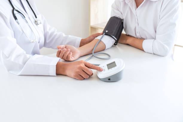 Doctor using Blood pressure monitor and stethoscope checking measuring arterial blood pressure on arm to a patient in the hospital, healthcare and medical concept stock photo