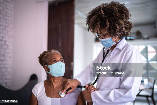 Doctor using listening senior patient heartbeat during a home visit - using a face mask