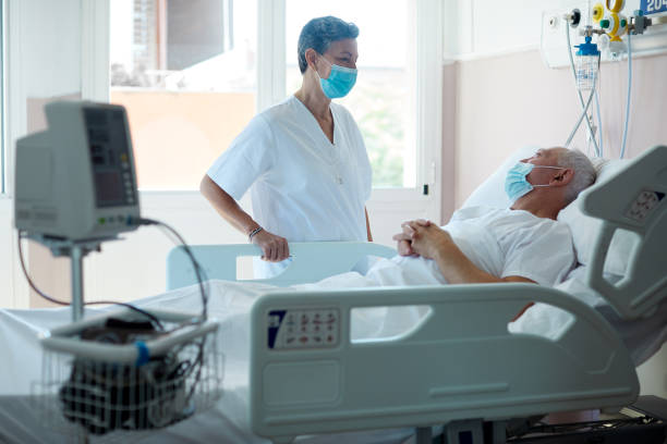 A doctor visiting a patient in a hospital ward. Hospital COVID patient in hospital bed stock pictures, royalty-free photos & images