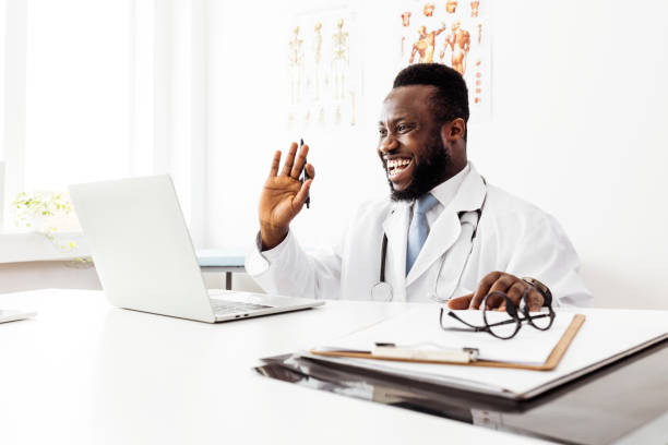 Doctor Waving for Video Call on Laptop in Clinic Doctor Waving for Video Call on Laptop in Clinic doctor of physio therapy online stock pictures, royalty-free photos & images