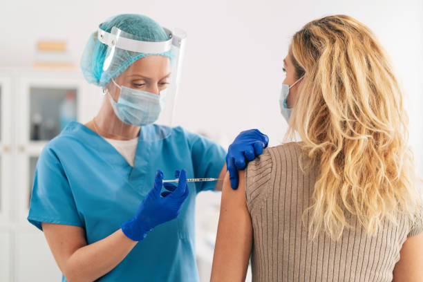 Doctor wearing protective face shield and surgical gloves injecting COVID-19 vaccine into patient's arm Doctor wearing protective work wear injecting vaccine into patient's arm anti vaccination stock pictures, royalty-free photos & images