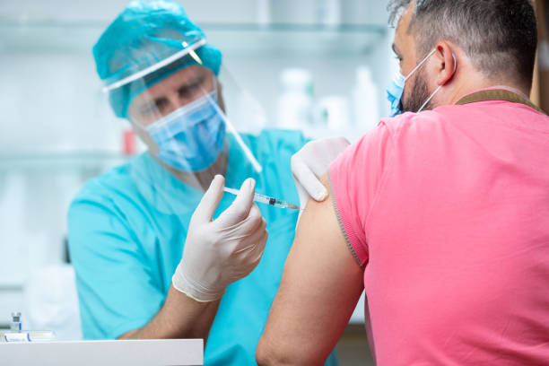 Doctor wearing protective workwear injecting vaccine into patient's arm Doctor wearing protective visor and surgical gloves injecting COVID-19 vaccine into patient's arm covid vaccine stock pictures, royalty-free photos & images