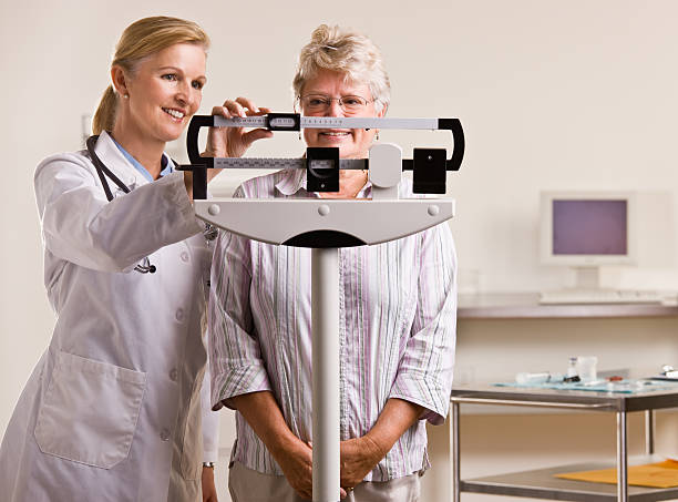 Doctor weighing senior woman stock photo