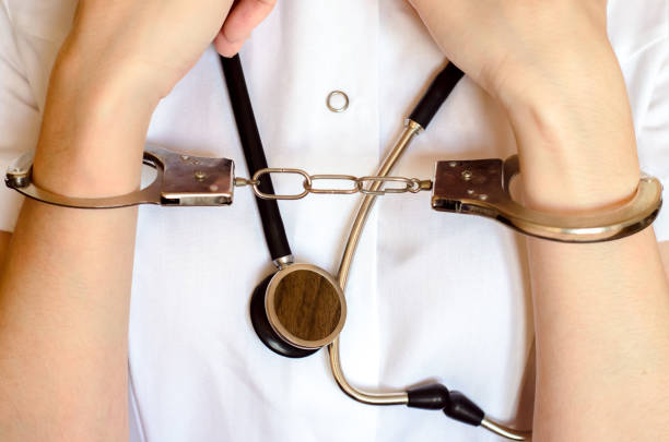 lekarz ze stetoskopem i ręką na kajdankach z bliska pojęcie błędu medycznego - błąd medyczny zdjęcia i obrazy z banku zdjęć