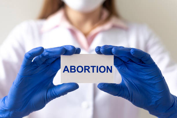 doctora mujer con guantes de protección sostiene un papel con aborto de texto - abortion clinic fotografías e imágenes de stock