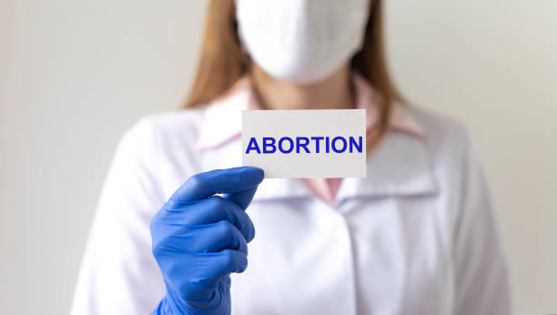 doctora mujer con guantes de protección sostiene un papel con aborto de texto - abortion clinic fotografías e imágenes de stock