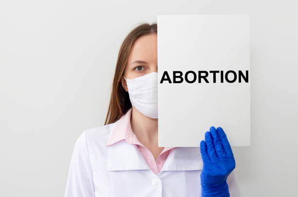 doctora mujer con máscara protectora y guantes sostiene un papel con aborto de texto - abortion clinic fotografías e imágenes de stock