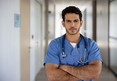 Portrait of a Latin American doctor in scrubs working at the hospital and looking at the camera with arms crossed - healthcare and medicine concepts