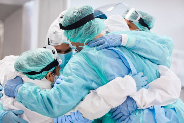 Doctors and nurses embracing each other during pandemic Medical professionals embracing each other in ICU. Doctors and nurses are in protective coveralls after successful treatment. They are at hospital during COVID-19. frontline worker stock pictures, royalty-free photos & images
