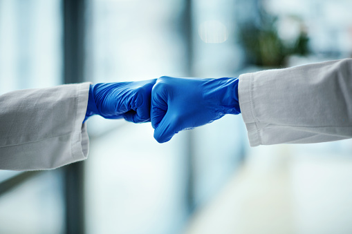 Side view of two unrecognizable doctors fist greeting in the hospital. Teamwork and cooperation is crucial to fight COVID-19 pandemic.