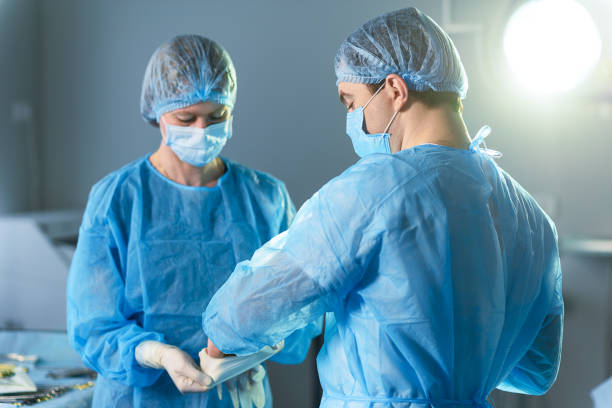 Doctors getting ready for operation Surgeon is wearing rubber glove with help of nurse. They are standing in orepation theatre evening gown stock pictures, royalty-free photos & images