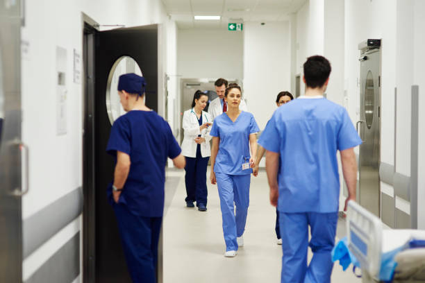 medici che camminano attraverso il corridoio in ospedale - hospital foto e immagini stock