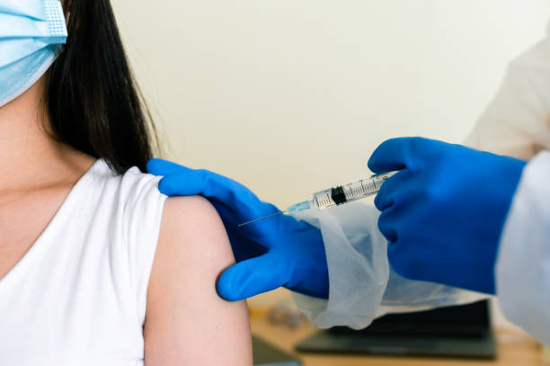 Doctors wearing PPE uniforms white gloves are inoculating the arm muscles to prevent COVID 19. stock photo