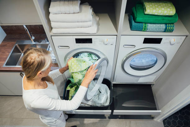 Doing Daily Laundry An aerial view of a mature woman as she puts her daily washing in the washing machine and doing some housework. utility room photos stock pictures, royalty-free photos & images
