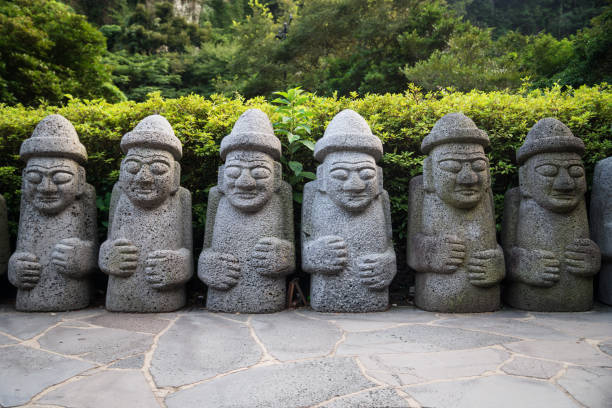 Dol Hareubang statues in a row in green forest, Seogwipo, Jeju Island, South Korea stock photo