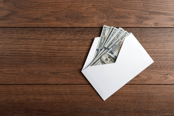 US dollars in a white envelope on a wooden table. The concept of income, bonuses or bribes. Corruption, salary, bonus. stock photo