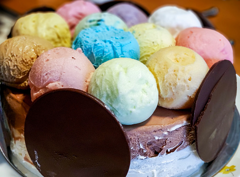 Dollops or scoops of ice cream in different colors and flavors form the highlights of upper portion of a dessert cake. Eating utensils located in the surrounding table area.