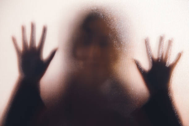 Domestic abuse victim with hands pressed against glass window stock photo