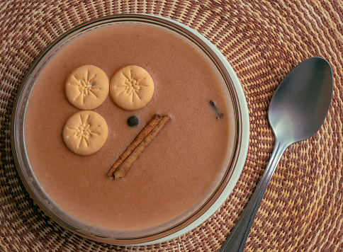Sweet beans served in a bowl with a woven tablecloth underneath, a dessert from the Dominican Republic made of red beans, milk, sugar and spices known as habichuelas con dulce.