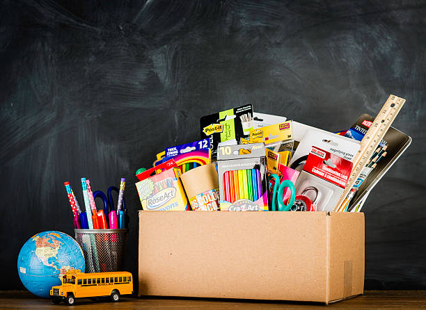 Donation Box for School Supplies "Suffolk, Virginia, USA - August 22, 2013: A horizontal studio shot of a a donation box for school supplies shot against an authentic school chalkboard. Next to the box is a miniature school bus, world globe and a collection of new pens and pencils." school supplies stock pictures, royalty-free photos & images