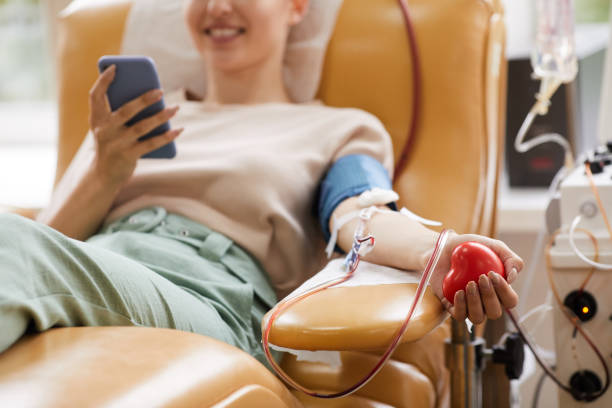 Donor donating blood Close-up of young woman lying on the couch with mobile phone while donating blood at the laboratory blood donation stock pictures, royalty-free photos & images