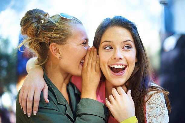 I don't believe it! That's such a juicy secret!! A young woman whispering a secret in her friend's ear whispering stock pictures, royalty-free photos & images