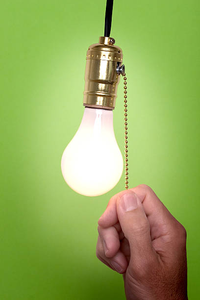 Don't forget to turn the light off! Hanging light bulb with pull switch.  Person is turning on or off the light. gchutka stock pictures, royalty-free photos & images