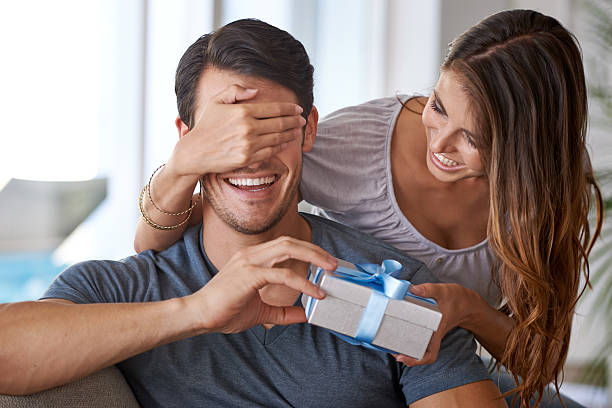 Don't peek! Shot of a young woman surprising her husband with a gift husband stock pictures, royalty-free photos & images