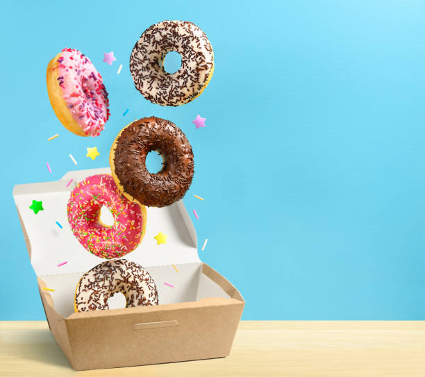 Donuts falling in paper box on blue background. Copy space Mix of multicolored sweet doughnuts falling in paper box on blue background. Copy space doughnut stock pictures, royalty-free photos & images