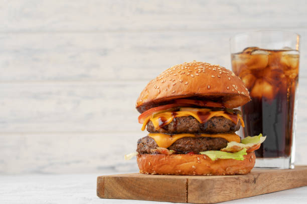 Double cheeseburger served on wooden board against white blurred background stock photo