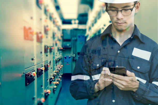 Double exposure of  Engineer or Technician man using smart phone for control electric in switch gear electrical room of oil and gas platform or plant industrial for monitor process, business and industry concept. stock photo
