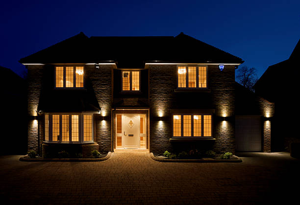 double fronted house at dusk a view of the front and driveway of a lovely double fronted luxury new home, taken at dusk with all of the interior and exterior lights switched on. The branding on the alarm box has been changed to a fictional text. stone house stock pictures, royalty-free photos & images