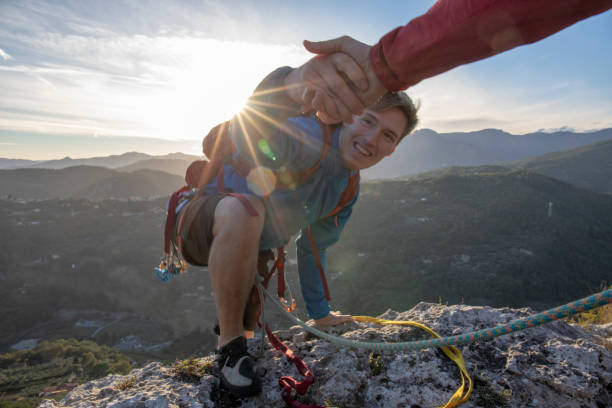 POV down arm to young man climbing up a rock face The sun is rising over the distant hills rock face stock pictures, royalty-free photos & images