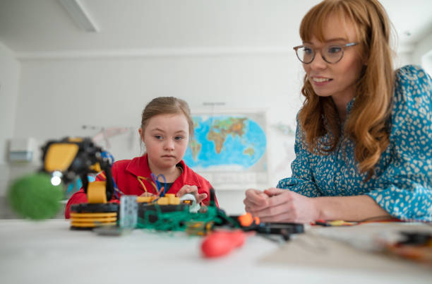 Down syndrome schoolgirl learning about robotics of teacher during class at school, integration concept. stock photo