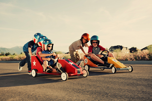 A group of young neighborhood boys race their go-carts for the street championship.