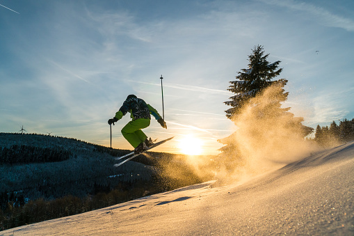 Downill skier jumping over natural kicker in beautiful powder snow and sunset conditions