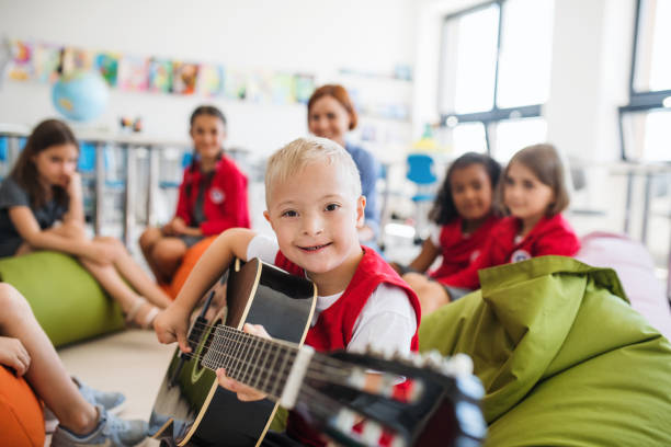 A down-syndrome boy with school kids and teacher sitting in class, playing guitar. A down-syndrome boy with school kids and teacher sitting on the floor in class, playing guitar. disability stock pictures, royalty-free photos & images