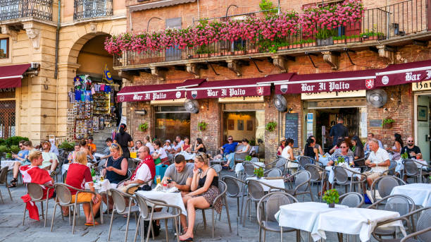 Dozens of tourists enjoy life in a typical café in Piazza del Campo in the medieval heart of Siena stock photo