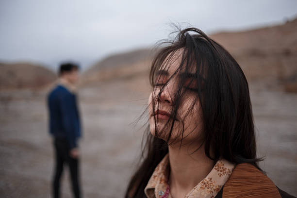 Dramatic portrait of a young brunette girl in cloudy weather. somewhere behind her, out of focus, her young lover boyfriend leaves her after break up . selective focus, small focus area stock photo