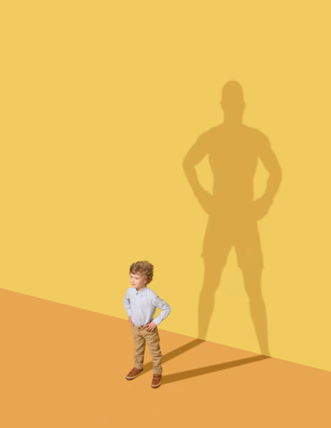 Dream about box I could protect my family. Future champion. Childhood and dream concept. Conceptual image with child and shadow on the yellow studio wall. Little boy want to become a boxer and to build a sport career. large stock pictures, royalty-free photos & images