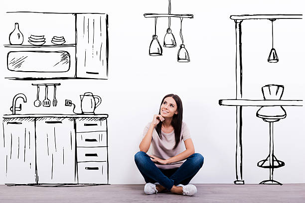 Dreaming about new kitchen. Cheerful young woman smiling while sitting on the floor against white background with drawn kitchen dreaming stock pictures, royalty-free photos & images